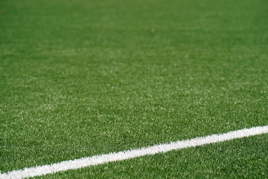 Close-up view of a green artificial soccer field with a white boundary line and space for text.
